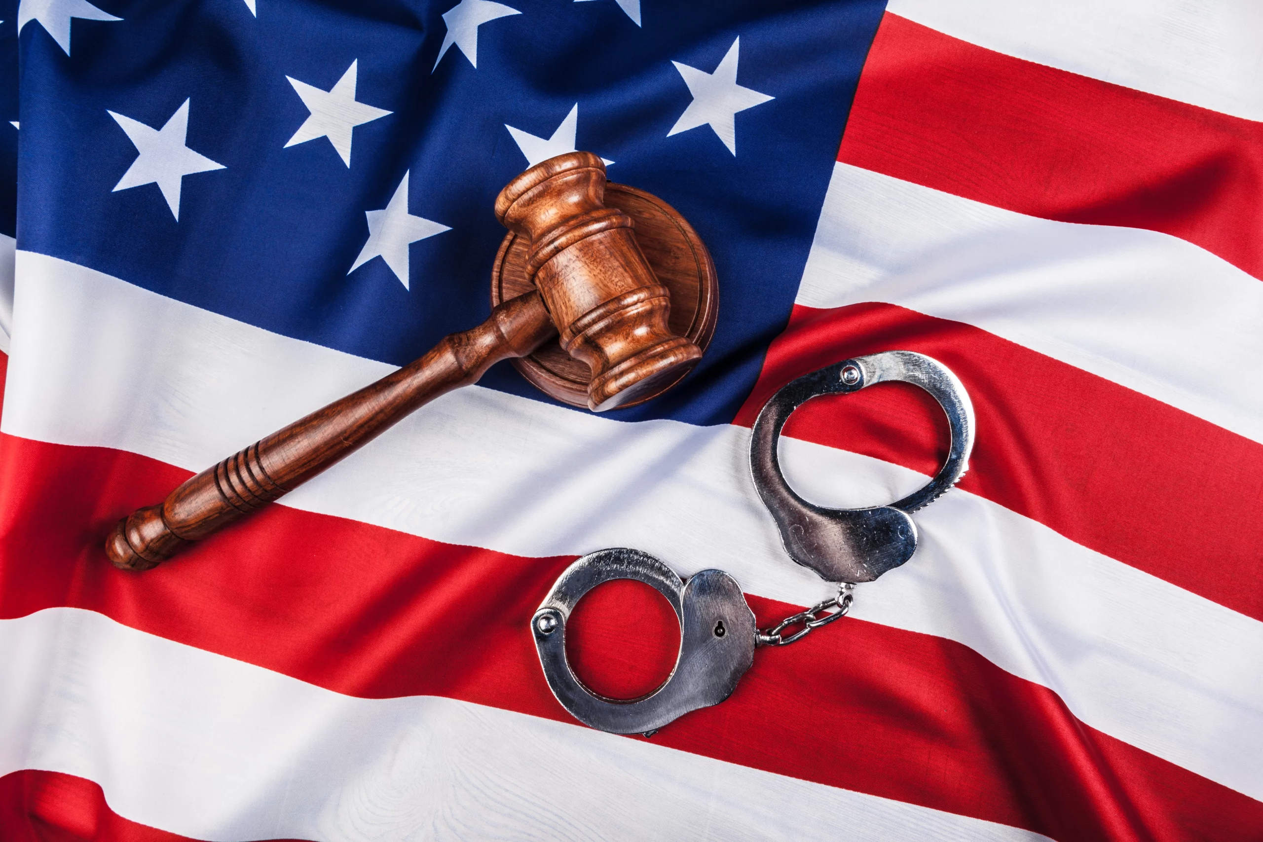 Wooden gavel and metal handcuffs resting on an American flag, symbolizing justice, law enforcement, and the tension between federal and state criminal charges.