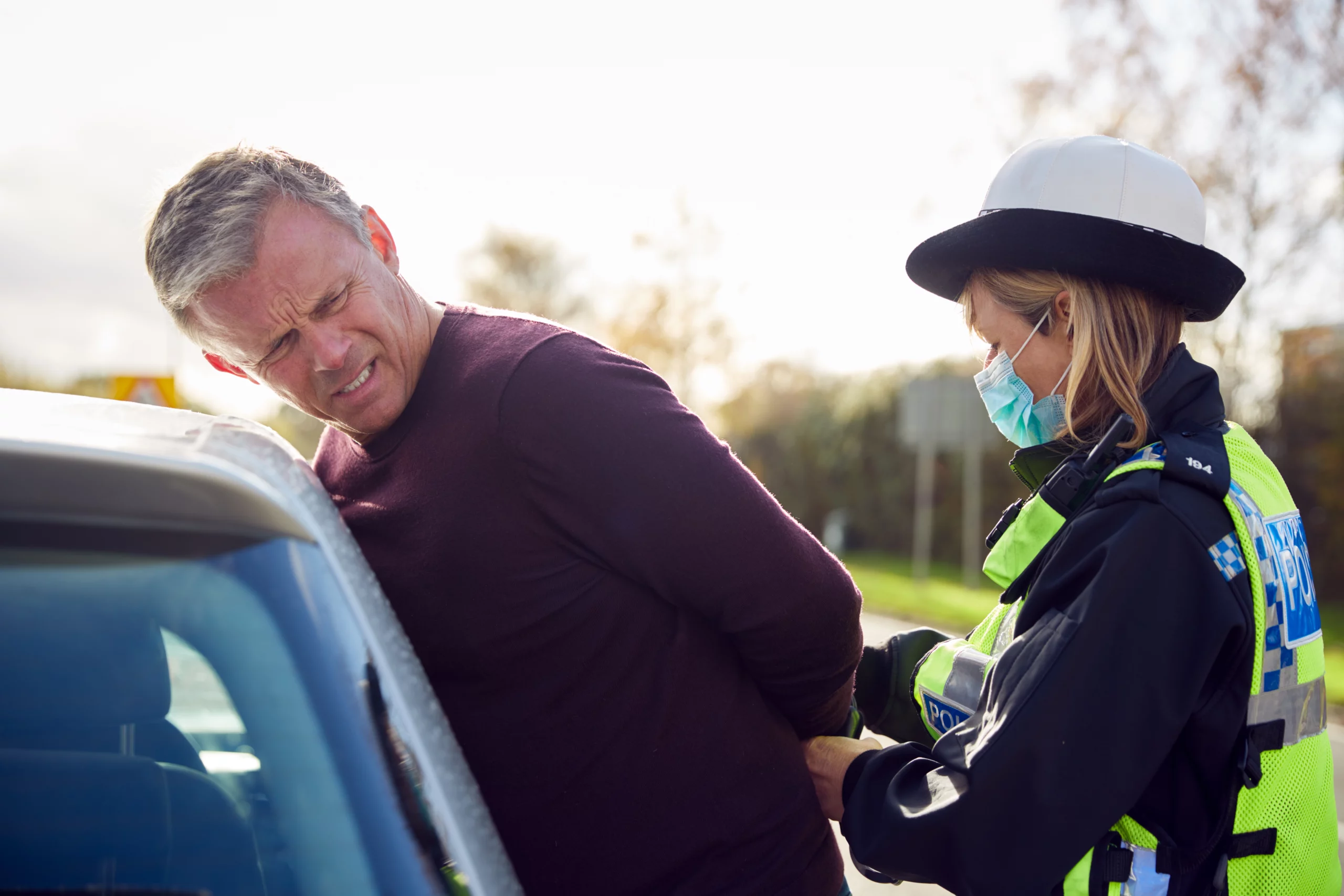Masked police officer handcuffing a man against a car in daylight, conveying tension and the risk of resisting arrest in Texas.
